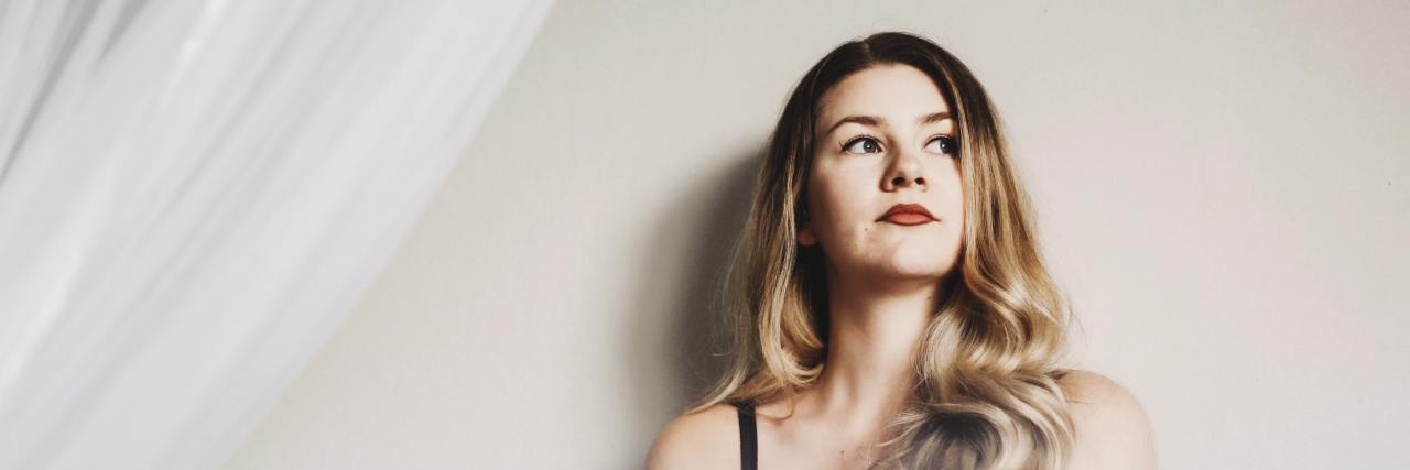 photo of woman sitting on bed against a plain wall, looking off-camera