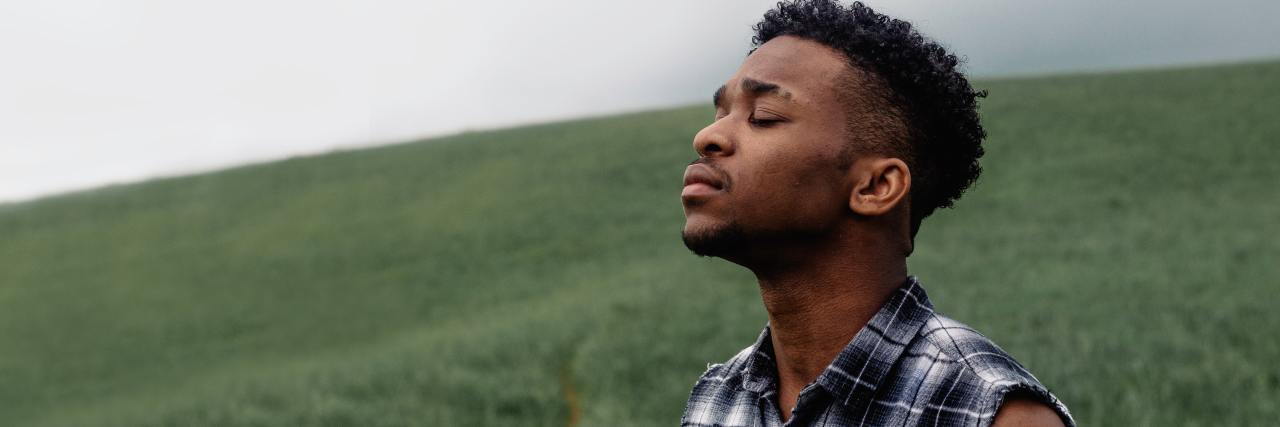 20 Affirmations and Readings For Folks Raised in Anti-LGBTQ+ photo of man standing on grassy hill with his eyes closed, head raised to the sky as if in prayer