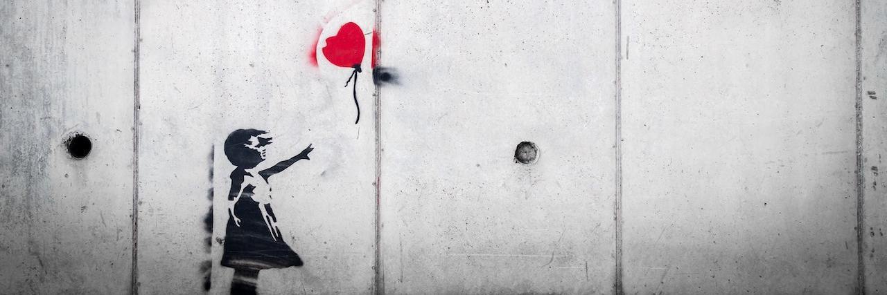 Painting on a white wall showing a side view of a young girl releasing a red, heart-shaped balloon