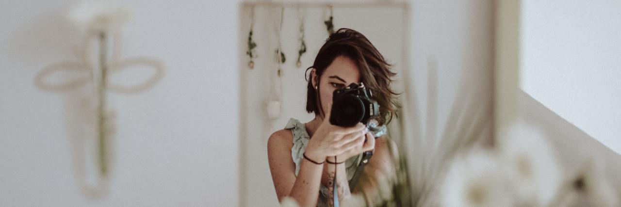 Dissociative Identity Disorder: My Parts and Their Roles in My Life photo of woman taking a photo of herself from a reflection in a mirror, which rests near some white flowers