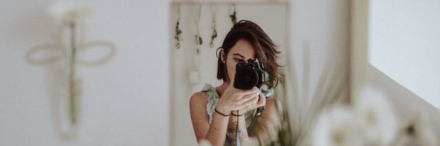 photo of woman taking a photo of herself from a reflection in a mirror, which rests near some white flowers