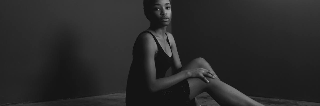 What to Know: The Link Between Sexual Abuse, Black Girls and Prison black and white photo of woman sitting on floor of room with bare walls, looking into the camera with sad expression