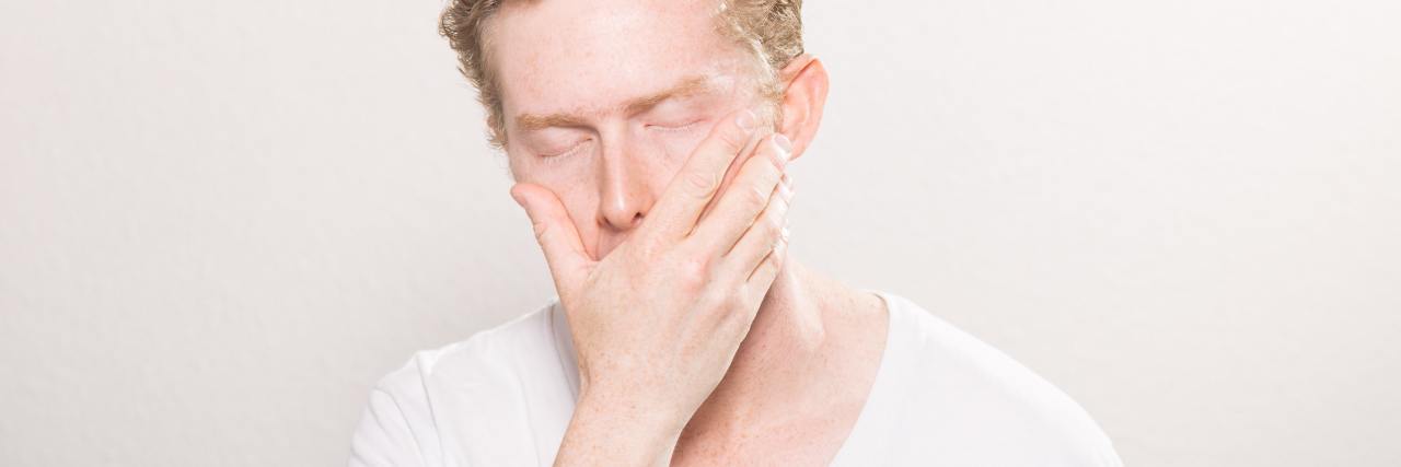 Why Lying About My Mental Illness Was So Unhealthy photo of man against white background with his eyes closed and his hand over his mouth
