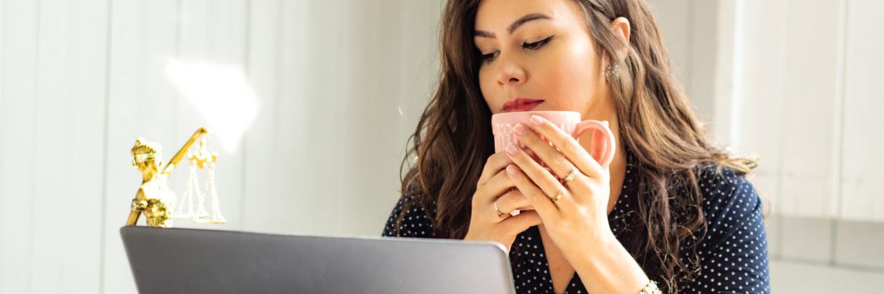 This Schedule Has Helped Me Cope During Coronavirus Lockdown photo of woman in front of laptop with a mug raised to her face