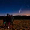 photo of group of people standing in a field looking at comet neowise in the distance just over the horizon