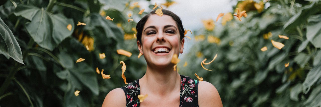 How You Can Help Those Recovering From Trauma A woman laughing outside surrounded by green leaves and showered with orange flower petals