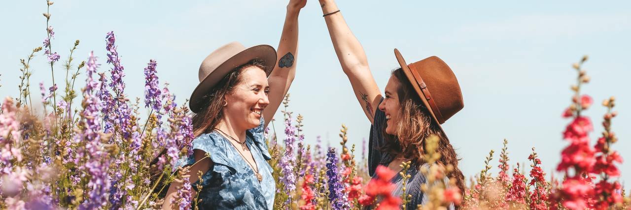 photo of two smiling women holding each other's hands up high in a flower field