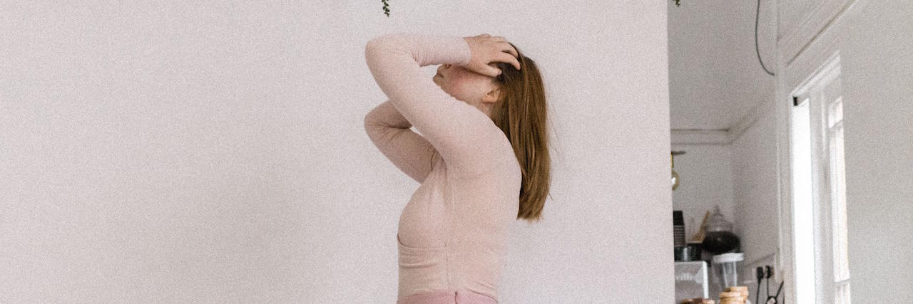 The Difference Between Being Triggered and Overwhelmed A woman standing in front of a wall with plants holding her head in her hands
