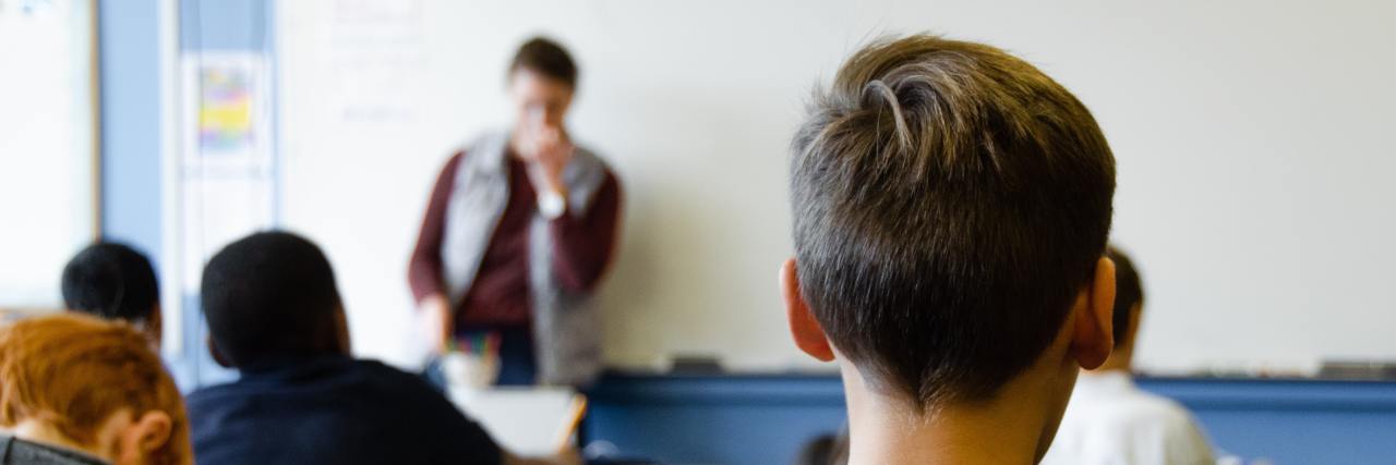 photo of young boy in class with teacher and other classmates in blurry background
