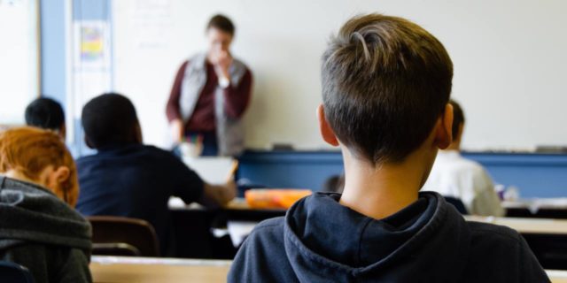 I’m a Teacher, and I’m Scared About Reopening Schools After COVID-19 photo of young boy in class with teacher and other classmates in blurry background