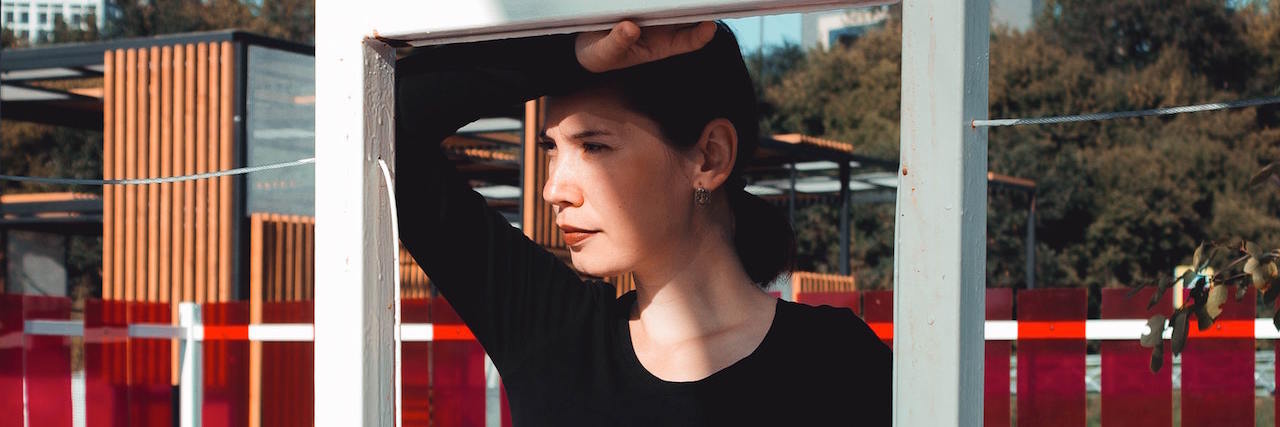 What No One Told Me About Life After Cancer A woman wearing black standing behind a white frame