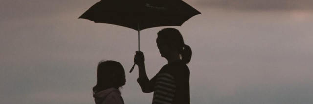 Mother holding umbrella over daughter