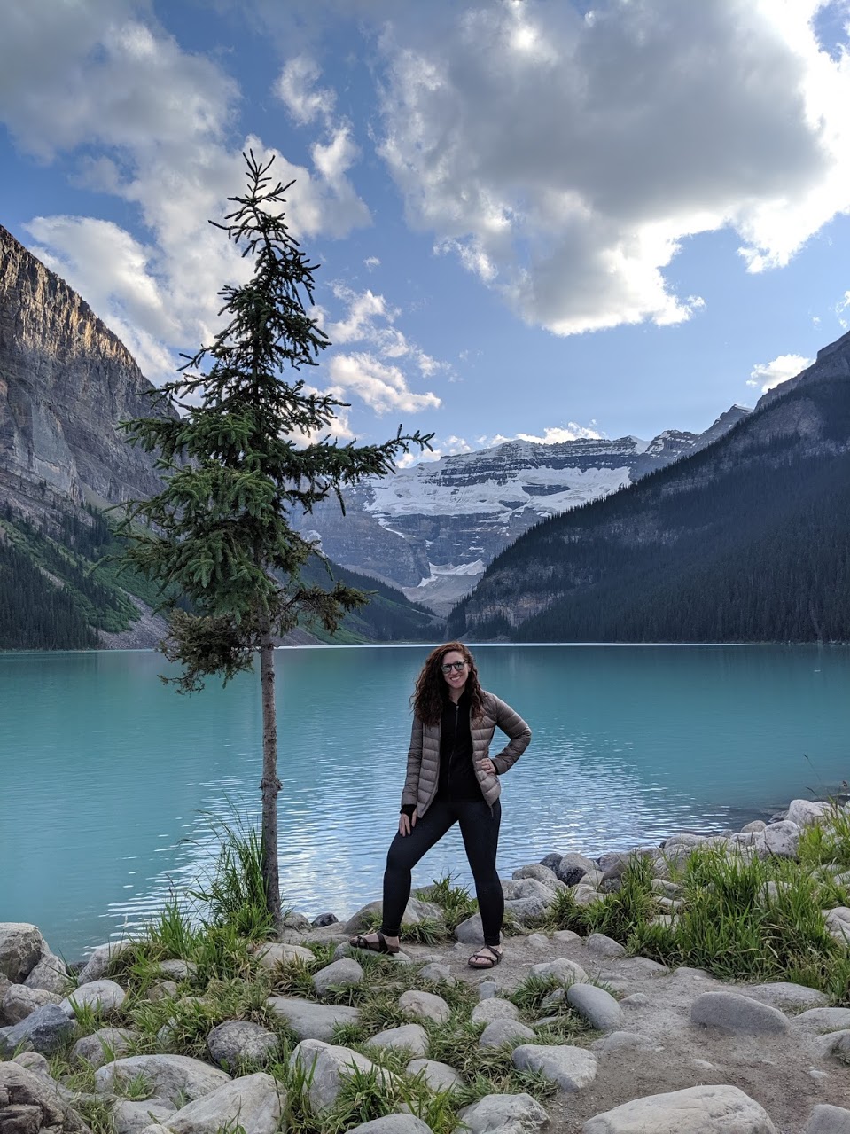 Jen standing in front of a beautiful blue lake with mountains in the background.
