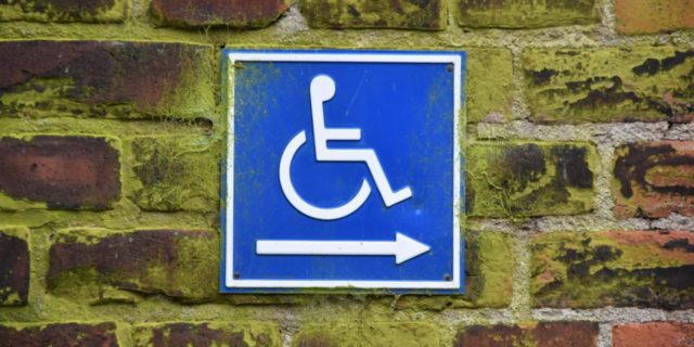 Accessibility sign with arrow, attached to mossy brick wall.