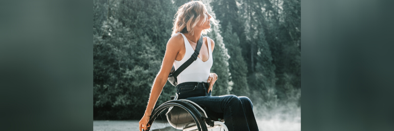 Your Wheelchair Fetish Doesn’t Empower Me Woman in a manual wheelchair with forest in the background.