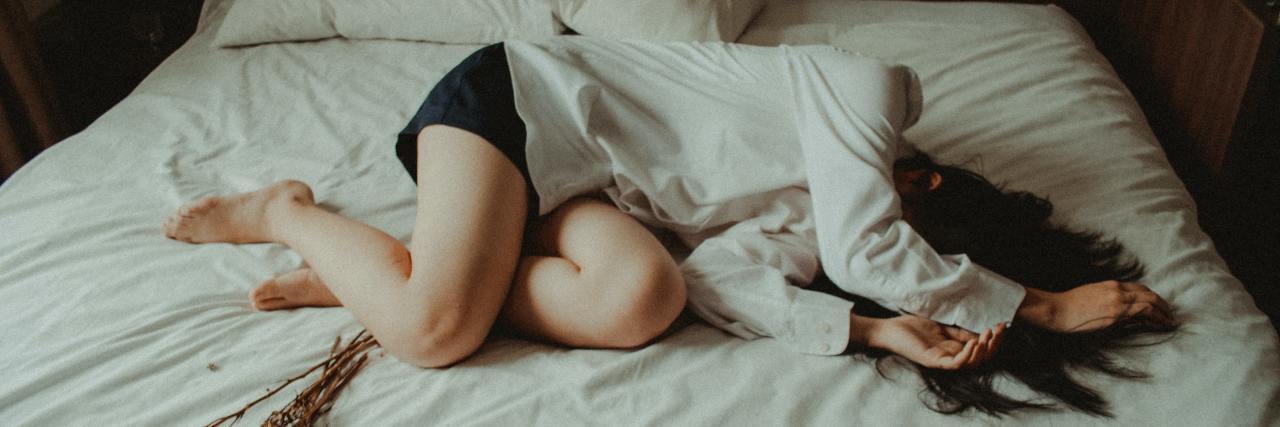 Mitochondrial Disease: Living With an Incurable Disease Woman laying on bed with arms over her head