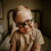 Madison's son smiling. He has Down syndrome and wears black framed eyeglasses.