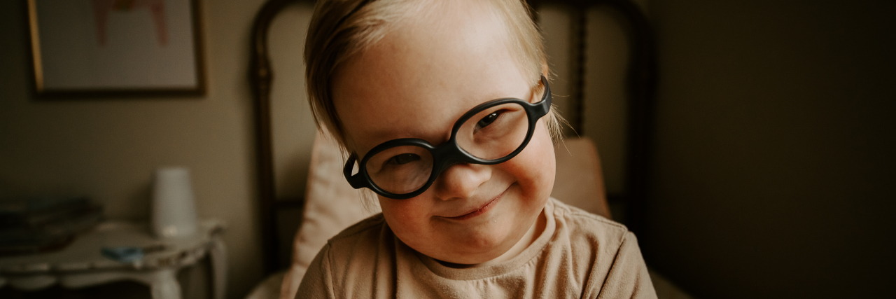 Madison's son smiling. He has Down syndrome and wears black framed eyeglasses.