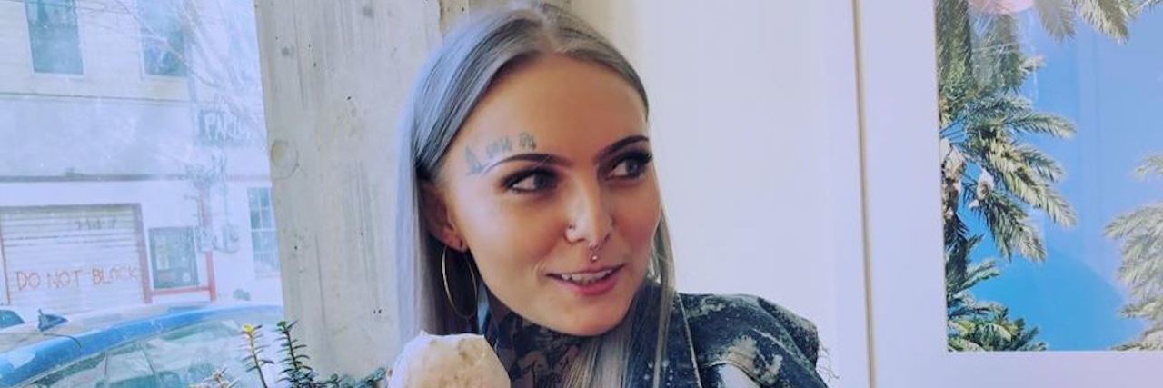 Daisy Coleman, a young woman with long silver hair and tattoos, eating an ice cream cone