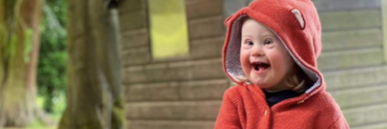 Girl With Down Syndrome Models New JoJo Maman Bébé Clothing Campaign Eleanor Manton, a young girl with Down syndrome, models a fox sweater while sitting on a rock in front of a rustic cabin