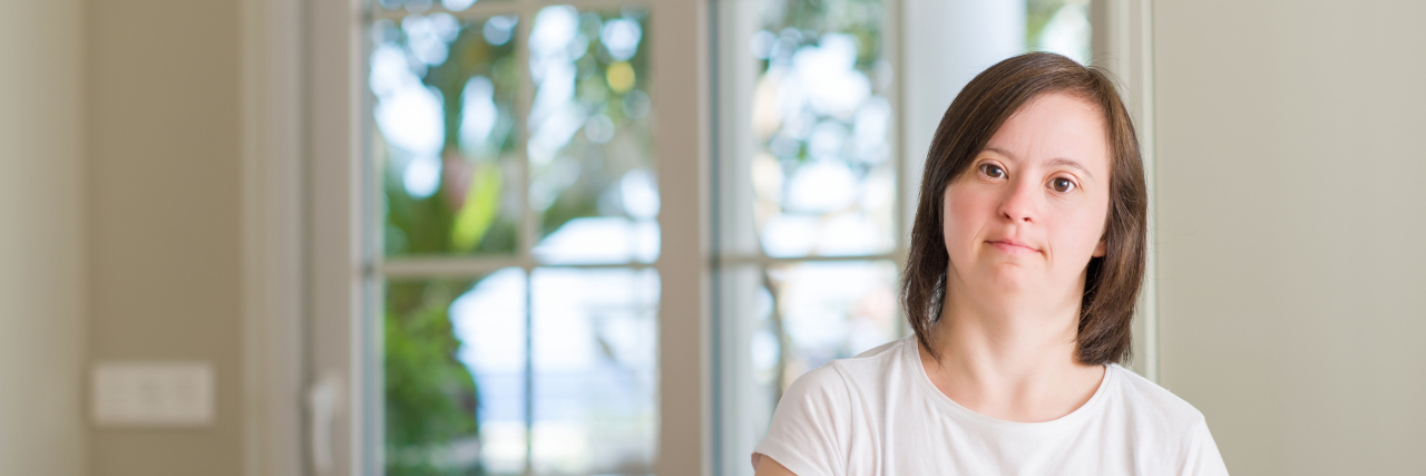 Don't Forget About People With Intellectual Disabilities Woman with Down syndrome at home with serious expression on her face.