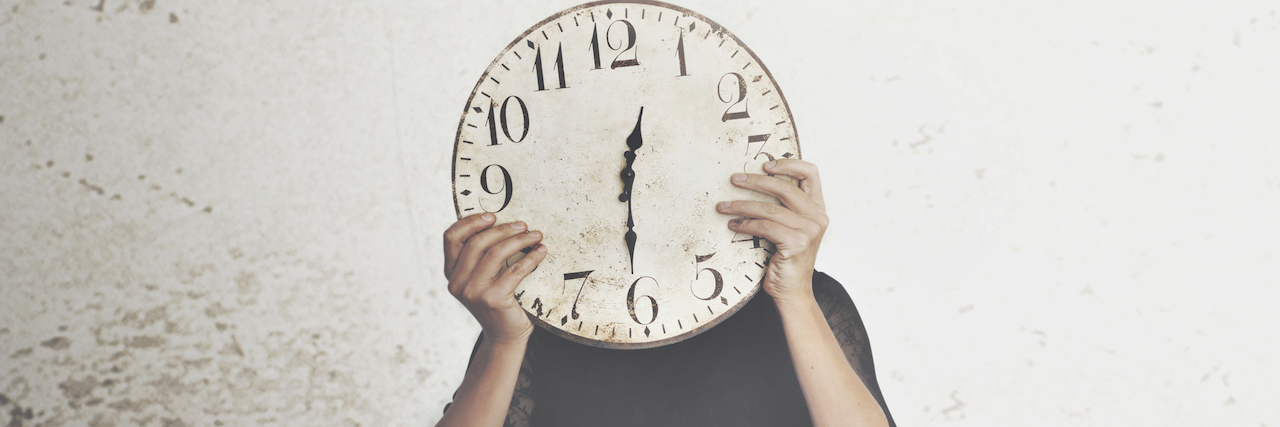 A woman holding a clock over her face