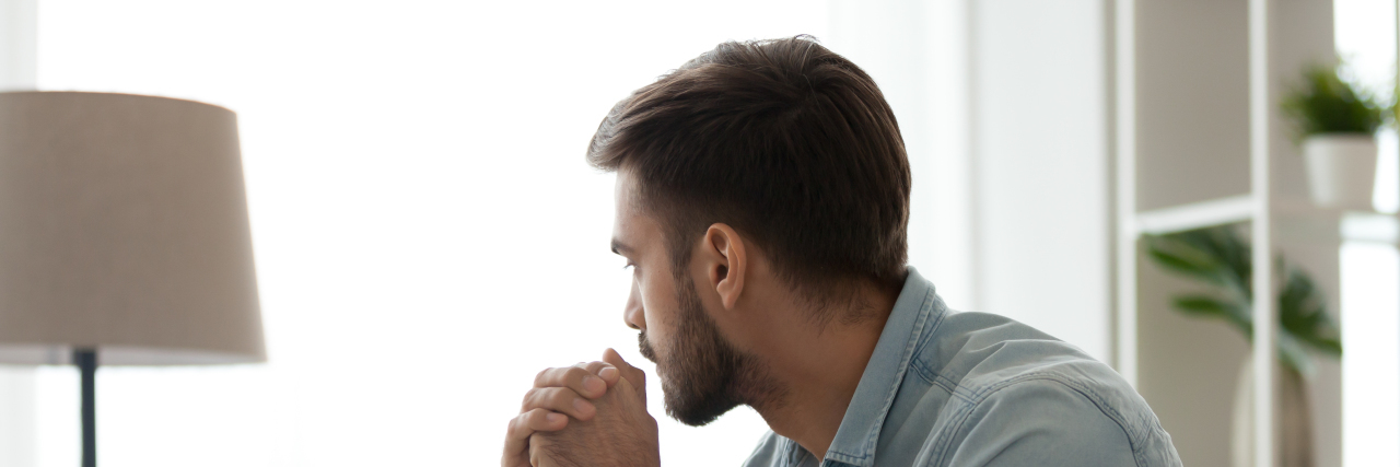 Feeling Unseen as a Person With Muscular Dystrophy During COVID-19 Serious man sitting on sofa alone at home, lost in thought.