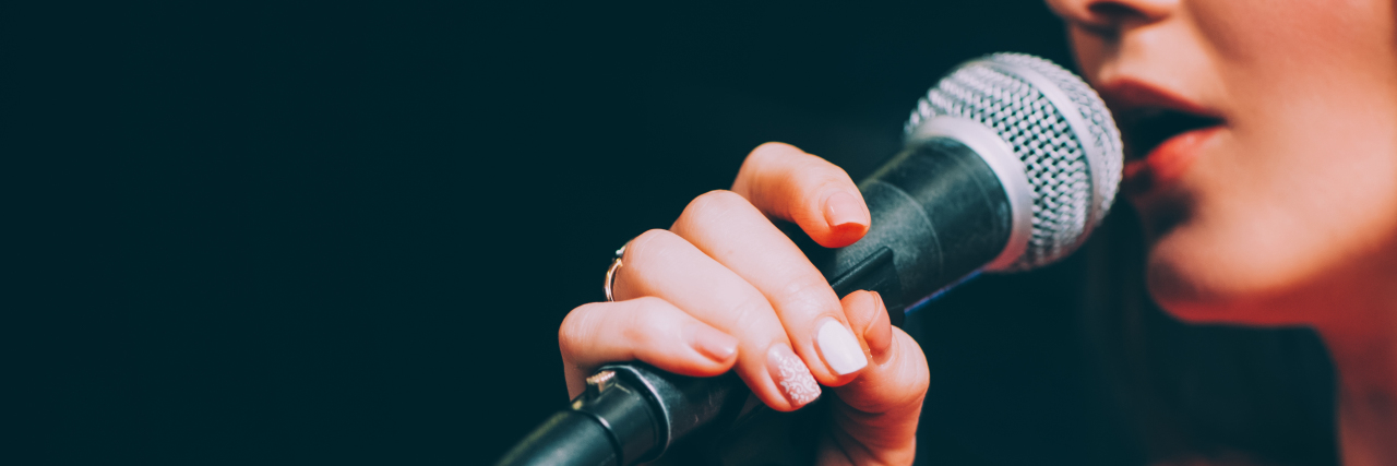 Being a Disabled Performer in an Ableist World Woman singing and holding microphone.