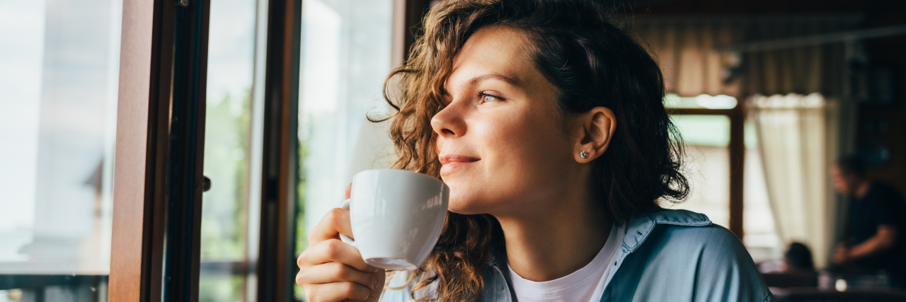10 Things I've Learned About Chronic Illness During COVID-19 Woman drinking coffee and looking out the window, sitting at table.