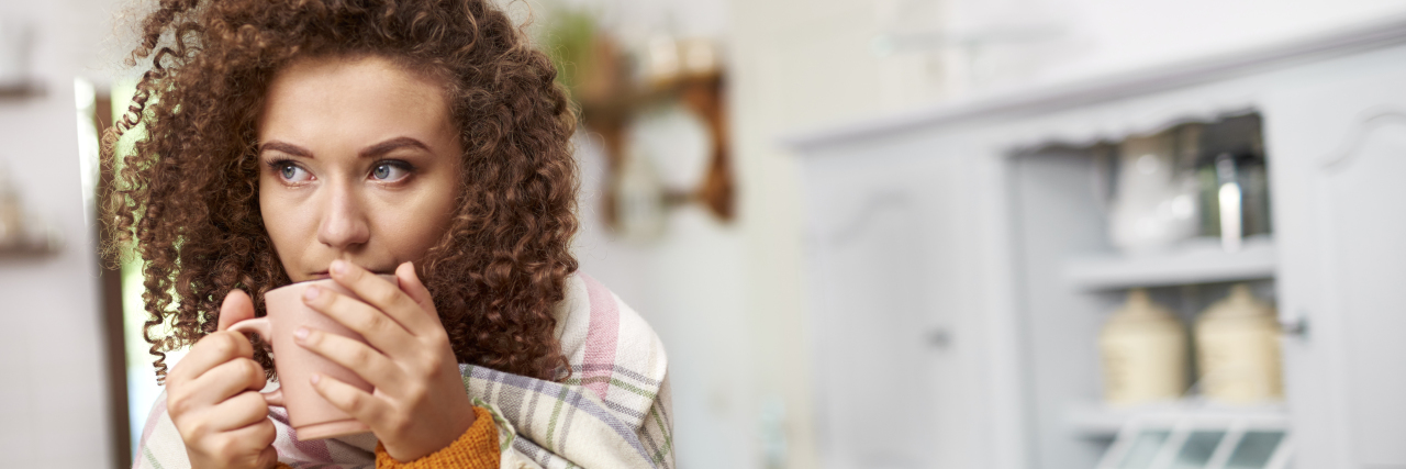 What Self-Care Looks Like With Hidradenitis Suppurativa Young woman wrapped in blanket drinking hot tea