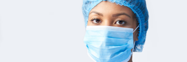 A Black female health care worker in scrubs and a face mask
