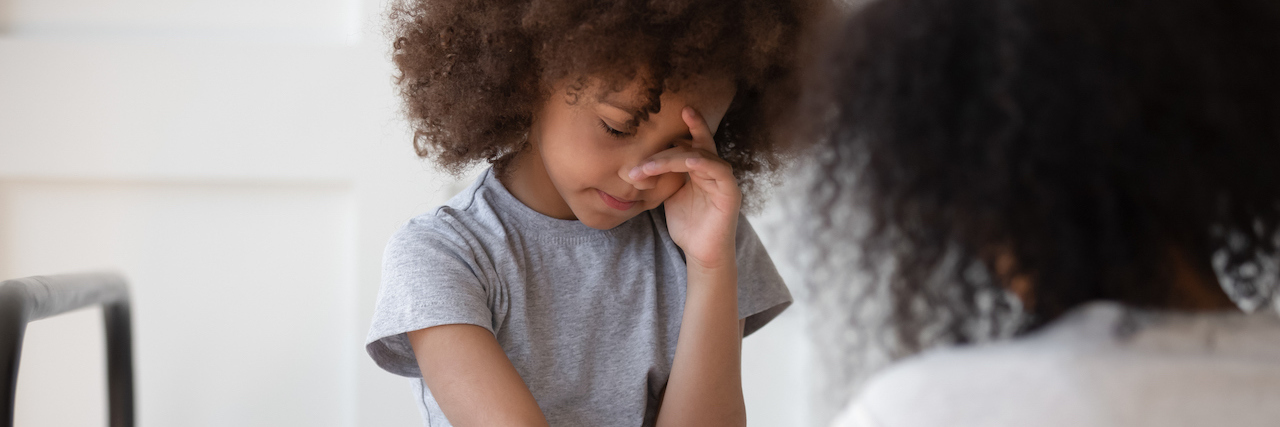 Autistic Children ‘Acting Out’ May be a Sign of Digestive Problems Young girl sitting on the bed looking upset with her hand on her face and her mom kneeling on the floor holding the girl's other hand