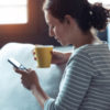 photo of woman with a mug and holding her phone with a serious expression