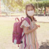 Asian girl wearing mask and carrying schoolbag with hand sanitizer.