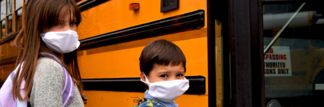 Two students wearing face masks board a school bus.