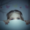 a little girl peaking from behind a bed
