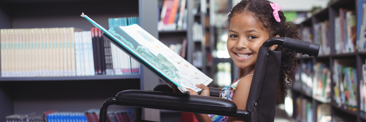 a girl in a wheelchair smiling at the library while holding a book