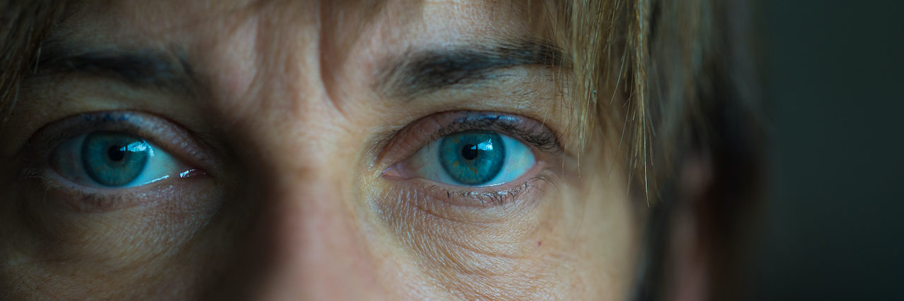 Portrait of mid aged woman with blue eyes, close up and selective focus on one eye, very shallow depth of field. Dark setting, toned image. (Portrait of mid aged woman with blue eyes, close up and selective focus on one eye, very shallow depth of fiel