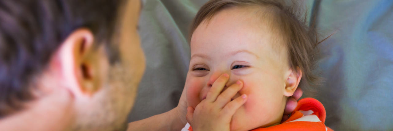 What I Would Tell My Past Self About Down Syndrome a dad smiling at a cute baby with Down syndrome
