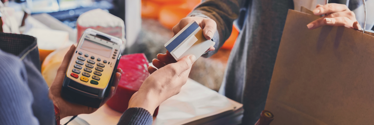 What It's Like Living With a Disability in a World Not Meant for Me a woman is giving a cashier an electronic form of payment