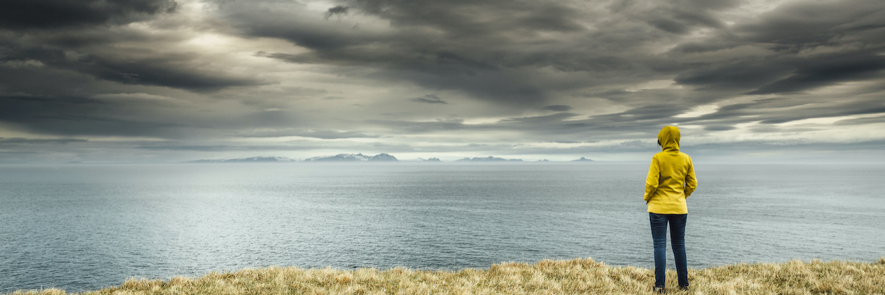 Finding Gratitude and Peace Amidst My Mental Health Struggles Woman standing under dark clouds looking out over a body of water