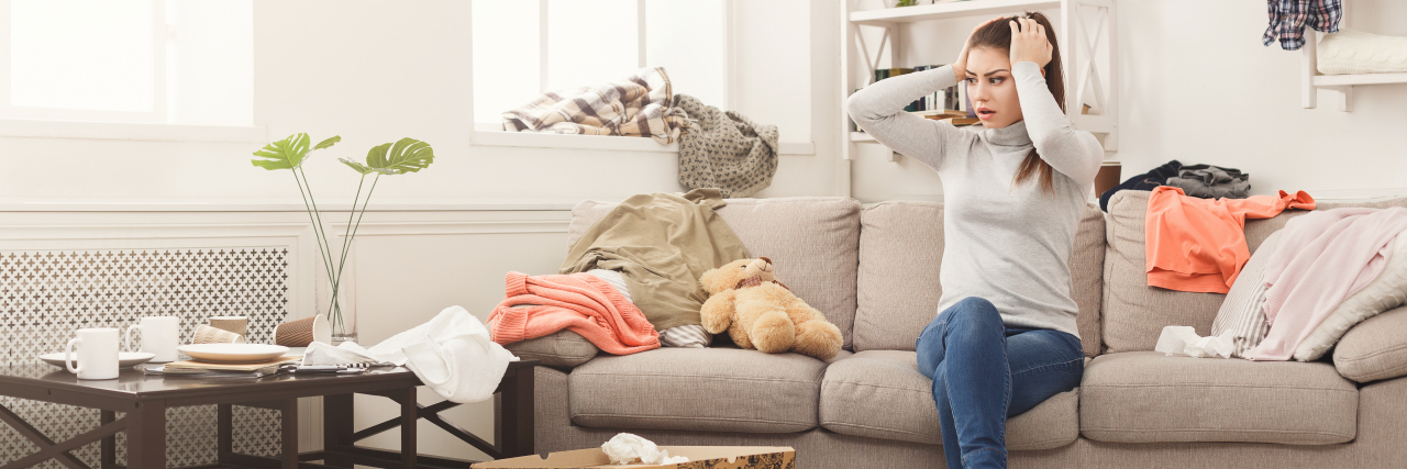 7 Things Considered 'Lazy' That Are Really Chronic Illness Self-Care Woman looking at messy living room.