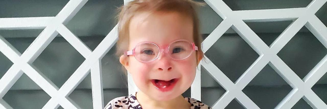 Adorable girl with Down syndrome wearing pink eyeglasses.