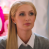Paris Hilton, wearing a white collared shirt, gray sweater and her long blonde hair pushed in front of one shoulder
