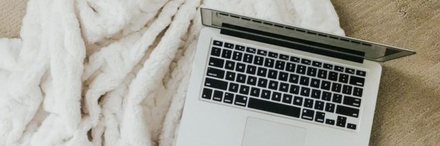 An open laptop on a fluffy white blanket on the floor