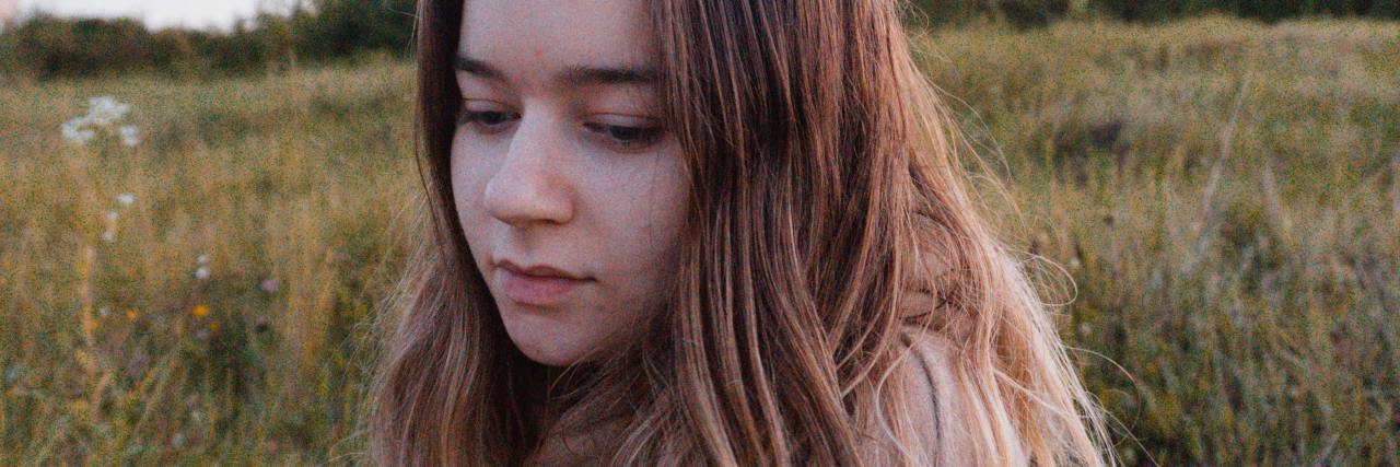 When My Therapist Finally Named This Part of My Childhood Abuse photo of young woman in field looking down, eyes closed, upset