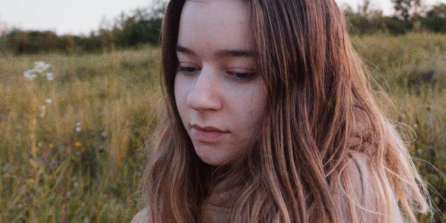 When My Therapist Finally Named This Part of My Childhood Abuse photo of young woman in field looking down, eyes closed, upset