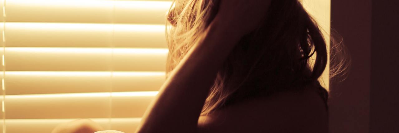 Struggling Without Mental Health Support During COVID-19 photo of woman sitting by window in golden light with hand in hair