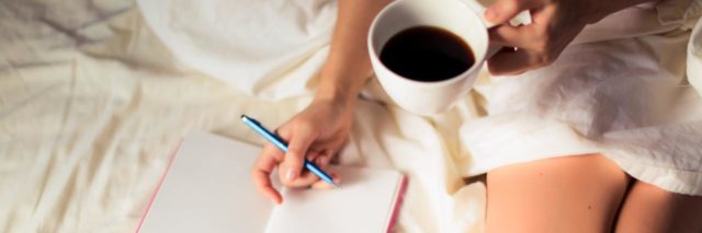 photo of woman sitting on bed with gratitude notebook and mug of coffee