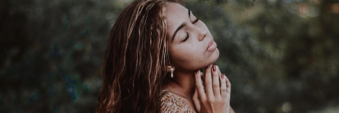 6 Types of Grief We Don't Talk About A woman standing outside, with her eyes closed and her hands clasped together